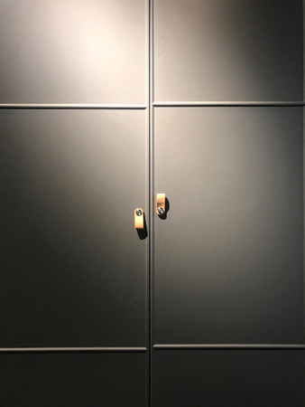 Black cabinet door with brown leather handle under warm light, front viewの写真素材