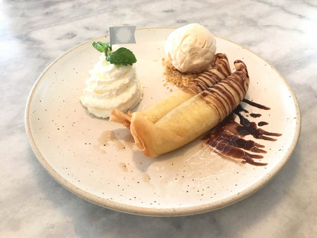 Deep fried of banana wrapped with dough sheet served with ice cream and whip cream topped with...