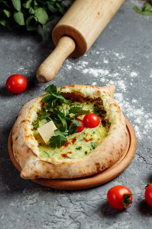 Adjarian khachapuri with cheese, spinach, tomatoes and herbs. On a gray-blue board Georgian cuisine. Flat lay. Top viewの写真素材