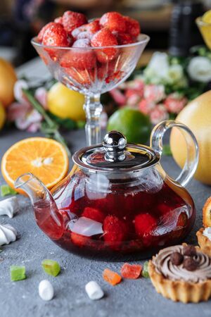 Glass teapot with fruit raspberry tea and mint on a blue background with fruits and decorations.の写真素材