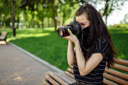 beautiful girl with a camera wears a medical mask and takes pictures in the park. Coronavirus 2019 nCoV pneumonia outbreakの写真素材