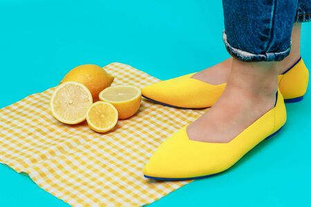 beautiful female legs are dressed in stylish yellow shoes without a heel. Light yellow summer sandals on a blue background against a background of bright lemons.の写真素材