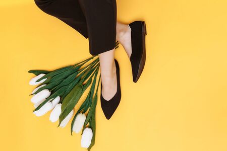 Beautiful female legs are dressed in stylish black flat shoes. black sandals on a yellow background.の写真素材