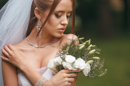Beautiful bride in a magnificent wedding dress posing among greenery on the street. Dvushka poses in...