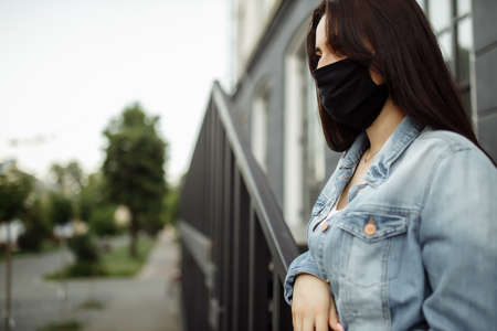 girl in a protective mask on a balcony looks at an empty city.の写真素材