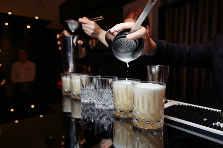 hands of a bartender holding a shaker pouring a drink into a glass.