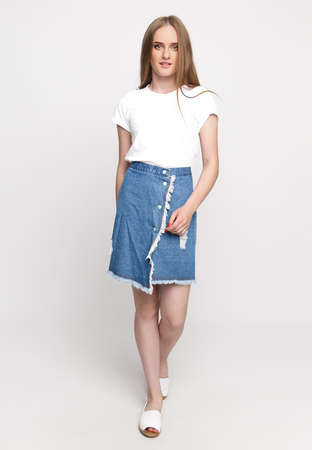 cute young slender woman in a white t-shirt and denim fashionable skirt on a white background. concept of advertising photo for once.