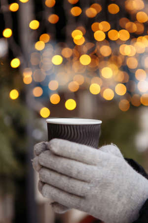 hands in mittens hold a hot cup of coffee. Coffee to go in winter.の写真素材