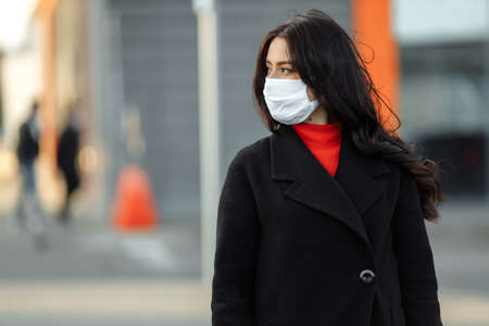 Portrait of beautiful woman walking on the street wearing protective mask as protection against infectious diseases. Attractive unhappy model with flu outdoors.の写真素材