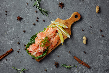 Pieces of fried salmon with dill and lemon wedges on a wooden board.