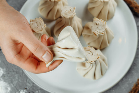 the hand holds the chikali by the tail. Khinkali in a Georgian restaurant in hand. Georgian cuisine.