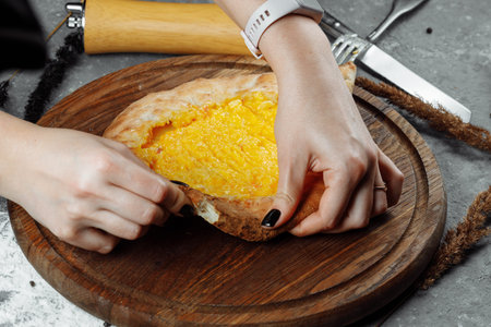 a young woman begins to eat fragrant khachapuri in ajarian with cheese on wooden support with a...