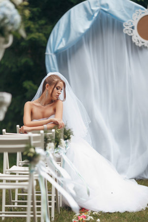 Beautiful bride in a magnificent wedding dress posing among greenery on the street. girl poses in a wedding dress for advertising. Bride concept for advertising dresses.の写真素材