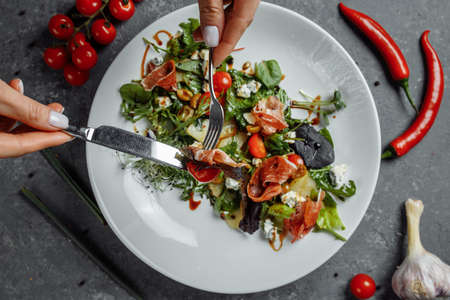 jamon salad, salad mix, spinach, pear, cherry tomatoes, Dor Blue, capers and vinegar dressing Bianco. Female hands holds fork and knifeの写真素材