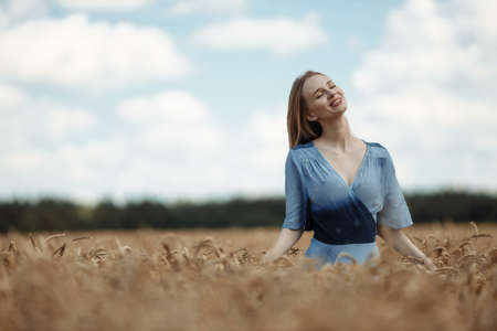 A beautiful young woman is walking in a wheat fieldの写真素材
