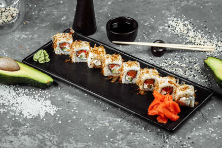 sushi rolls with cream cheese, fried salmon, tuna shavings or dried bonito, cucumber, nori. Chopsticks holding fresh katsuobushi roll in Japanese restaurant closeup.の写真素材