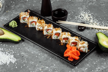 sushi rolls with cream cheese, fried salmon, tuna shavings or dried bonito, cucumber, nori. Chopsticks holding fresh katsuobushi roll in Japanese restaurant closeup.の写真素材