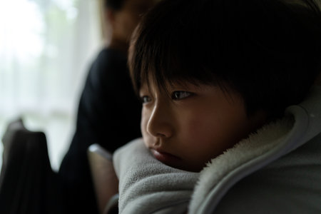 Portrait of asian boy sitting on sofa and looking at outsideの写真素材