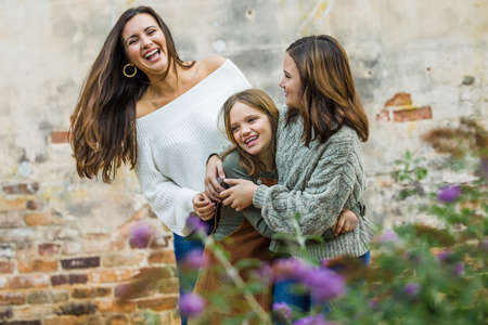 A young mom in her 30s with her two daughters outside hugging and laughing togetherの写真素材