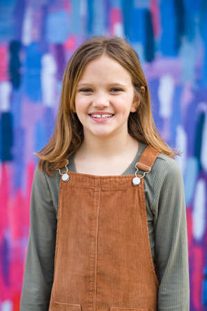 Young girl in a brown overall dress in the winter standing outside near a bright colored wallの写真素材