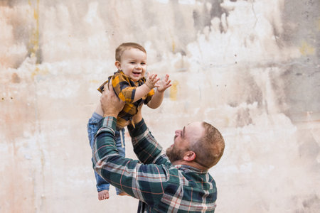 A father and his baby son outside in an urban setting against an old textured wall