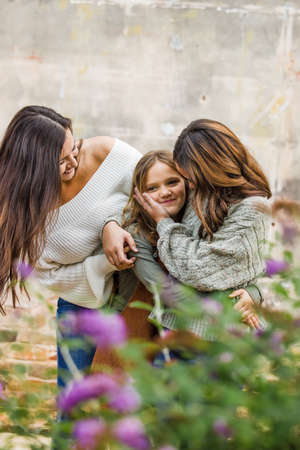 A young mom in her 30s with her two daughters outside hugging and laughing togetherの写真素材