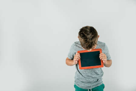 Little boy holding a red blank chalkboard sign with room for text and a message and blank space.の写真素材