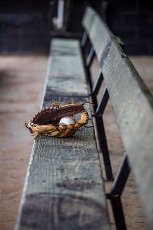 Empty dug out bench at a baseball field with a lone baseball glove and baseball sitting in the middle.の写真素材