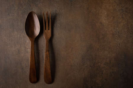 A rustic brown textured background with dark wood fork and spoon serving utensilsの写真素材