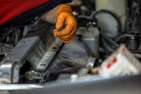 A man wearing an orange glove fixing and doing maintenace on a car engine in an auto repair shopの写真素材