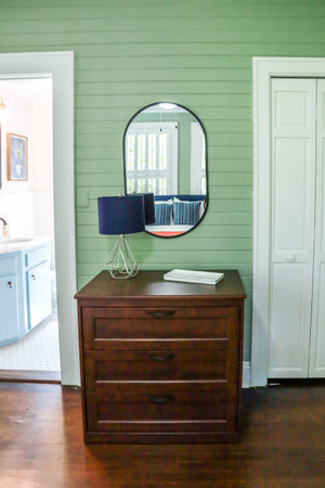 A simple dark wood stained dresser in a guest bedroom with green panel shiplap walls and a black...