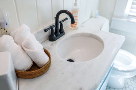 A basket of organized clean rolled white towels on a bathroom counter in a guest bathroom near a sink and toilet.の写真素材