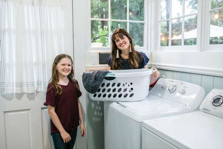 A mother and daughter doing laundry chores together in their natural light laundry roomの写真素材