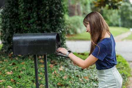 A teen brunette girl with long hair checking the mailbox for letters and packages.の写真素材