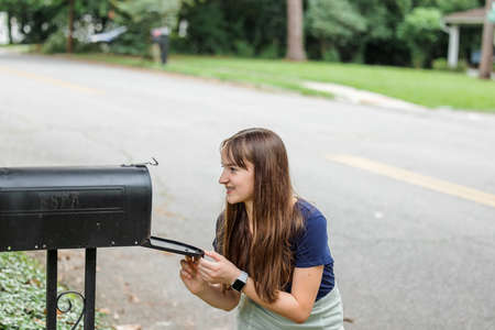 A teen brunette girl with long hair checking the mailbox for letters and packages.の写真素材