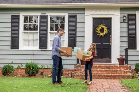 A father and daughter holding moving boxes outside a small blue cottage house getting ready for a moveの写真素材