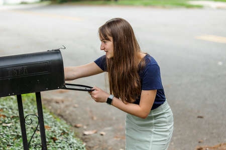 A teen brunette girl with long hair checking the mailbox for letters and packages.の写真素材