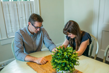 a woman and man praying at the kitchen table at home.