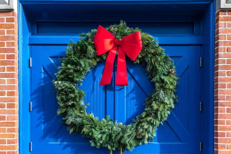 A large green outdoor Christmas holiday wreath with a bright red bow against a pair of bright cobalt blue doorsの写真素材