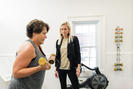 A female personal trainer helping a client exercise, train, and build muscle using small hand...
