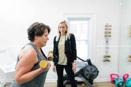 A female personal trainer helping a client exercise, train, and build muscle using small hand...