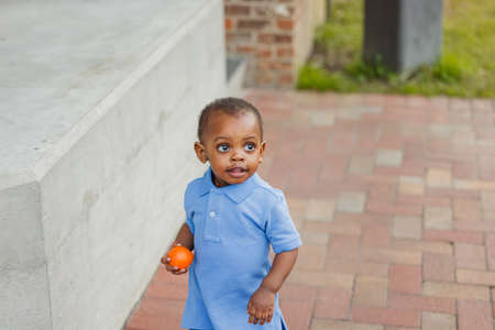 A cute one year old toddler African-American boy holding a healthy snack of an orangeの写真素材
