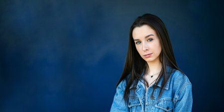 A beautiful teen brunette girl with a serious look and head tilt against a dark blue background with copy space as a bannerの写真素材