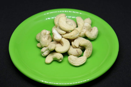 The pile of cashew nuts is on a black background on a green plate