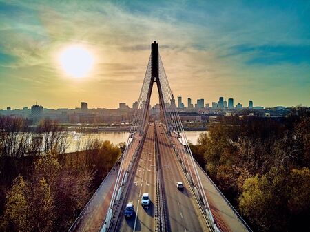 Beautiful panoramic aerial drone view to Swietokrzyski Bridge (English: Holy Cross Bridge) - is a cable-stayed bridge over the Vistula river in Warsaw, Poland in autumn November evening at sunsetの写真素材