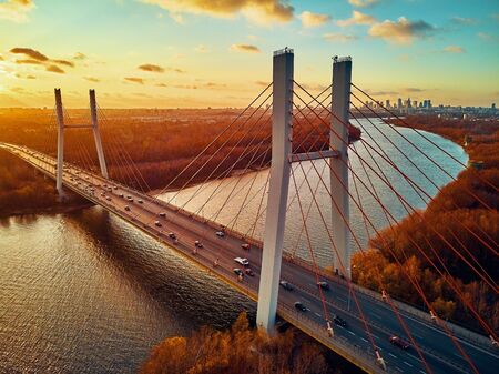 Beautiful panoramic aerial drone view to cable-stayed Siekierkowski Bridge over the Vistula river and Warsaw City skyscrapers, Poland in gold red autumn colors in November evening at sunsetの写真素材