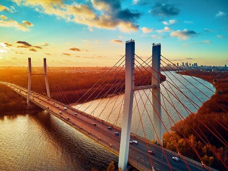 Beautiful panoramic aerial drone view to cable-stayed Siekierkowski Bridge over the Vistula river and Warsaw City skyscrapers, Poland in gold red autumn colors in November evening at sunsetの写真素材