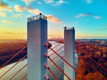 Beautiful panoramic aerial drone view to cable-stayed Siekierkowski Bridge over the Vistula river and Warsaw City skyscrapers, Poland in gold red autumn colors in November evening at sunsetの写真素材