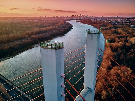 Beautiful panoramic aerial drone view to cable-stayed Siekierkowski Bridge over the Vistula river and Warsaw City skyscrapers, Poland in gold red autumn colors in November evening at sunsetの写真素材