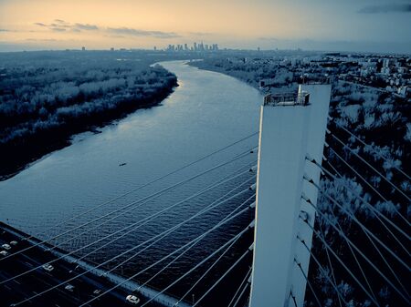 Beautiful panoramic aerial drone view to cable-stayed Siekierkowski Bridge over the Vistula river and Warsaw City skyscrapers, Poland in gold red autumn colors in November evening at sunsetの写真素材